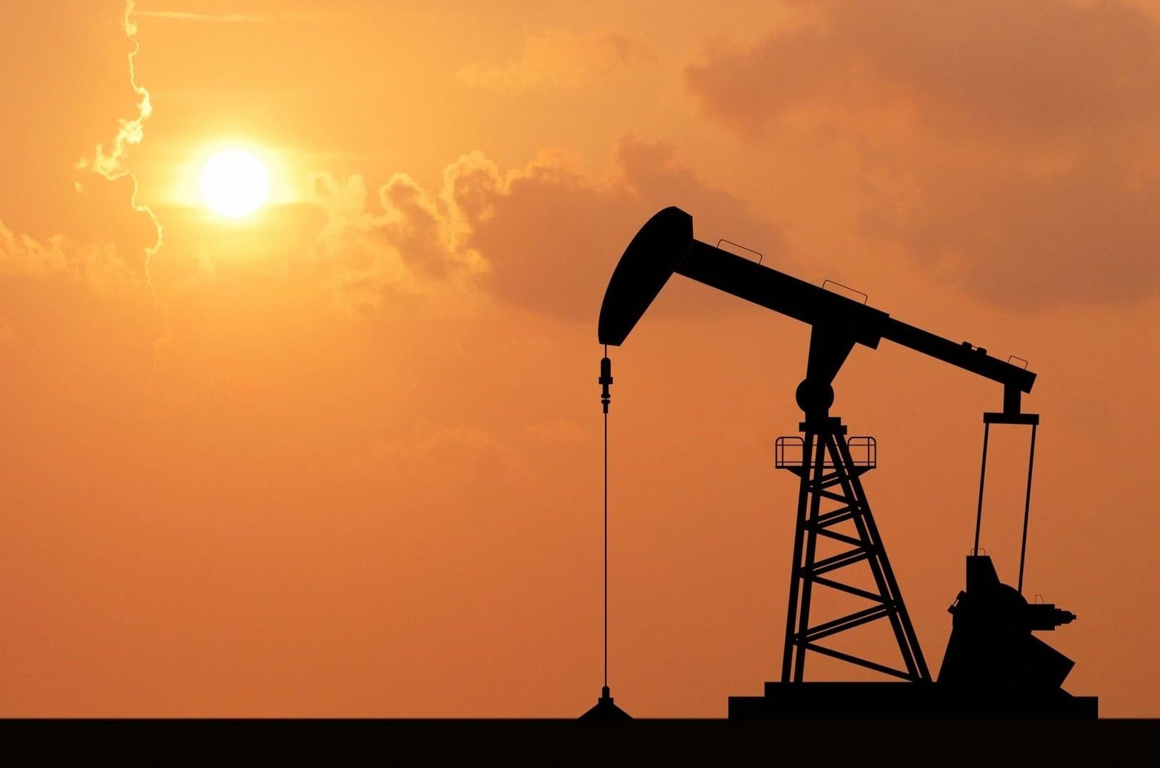 A silhouette of an oil well with the sun setting behind it.